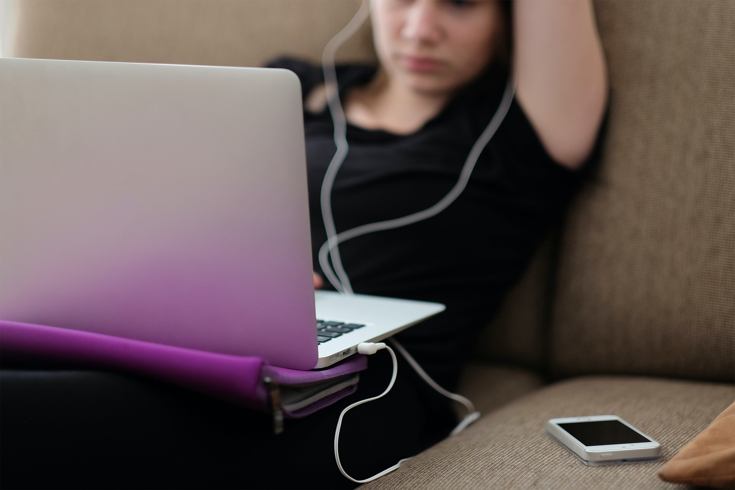 Eine junge Frau sitzt zuhause auf einer Couch. Sie hat einen Laptop auf Ihre Knie gelegt und Kopfhörer auf den Ohren. Sie hört konzentriert zu und versucht sich etwas einzuprägen.