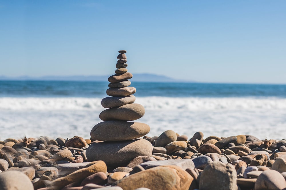 Gestapelte Steine an einem steinigen Strand, See oder Meer im Hintergrund
